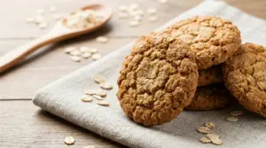 Biscotti all’avena croccanti su un canovaccio, con fiocchi d’avena sparsi e cucchiaio di legno sullo sfondo