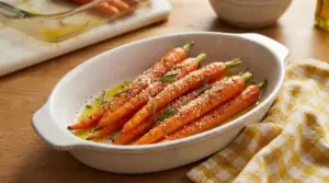 Carote al forno condite con olio, rosmarino e formaggio grattugiato in una pirofila bianca