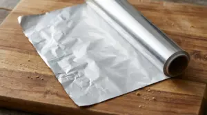 Rotolo di foglio di alluminio srotolato su un tagliere di legno, con lato opaco e lucido visibili